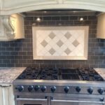 Ceramic kitchen backsplash with center framed inset of white square tiles arranged on diagonal with patterned accent tiles